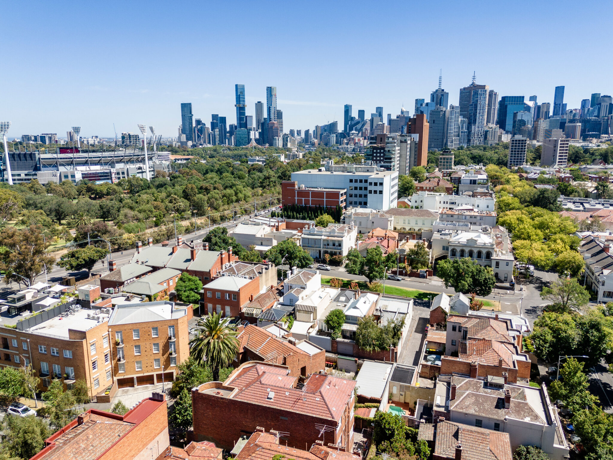 Aerial view over East Melbourne rooftops towards the MCG and the Melbourne city skyline
